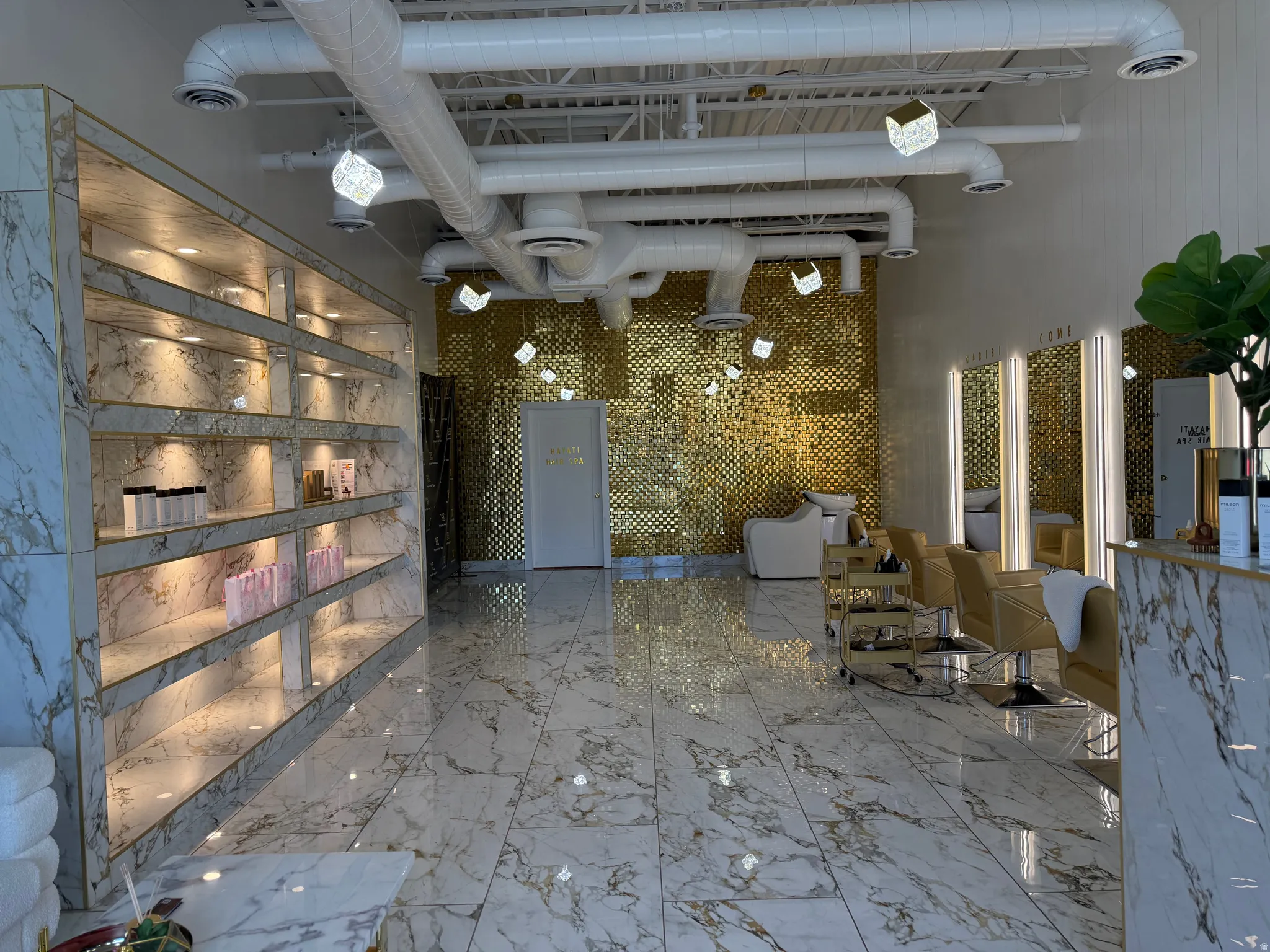 Spacious interior featuring large format marble-look tile flooring, an exposed white ductwork ceiling, and built-in shelving with integrated lighting