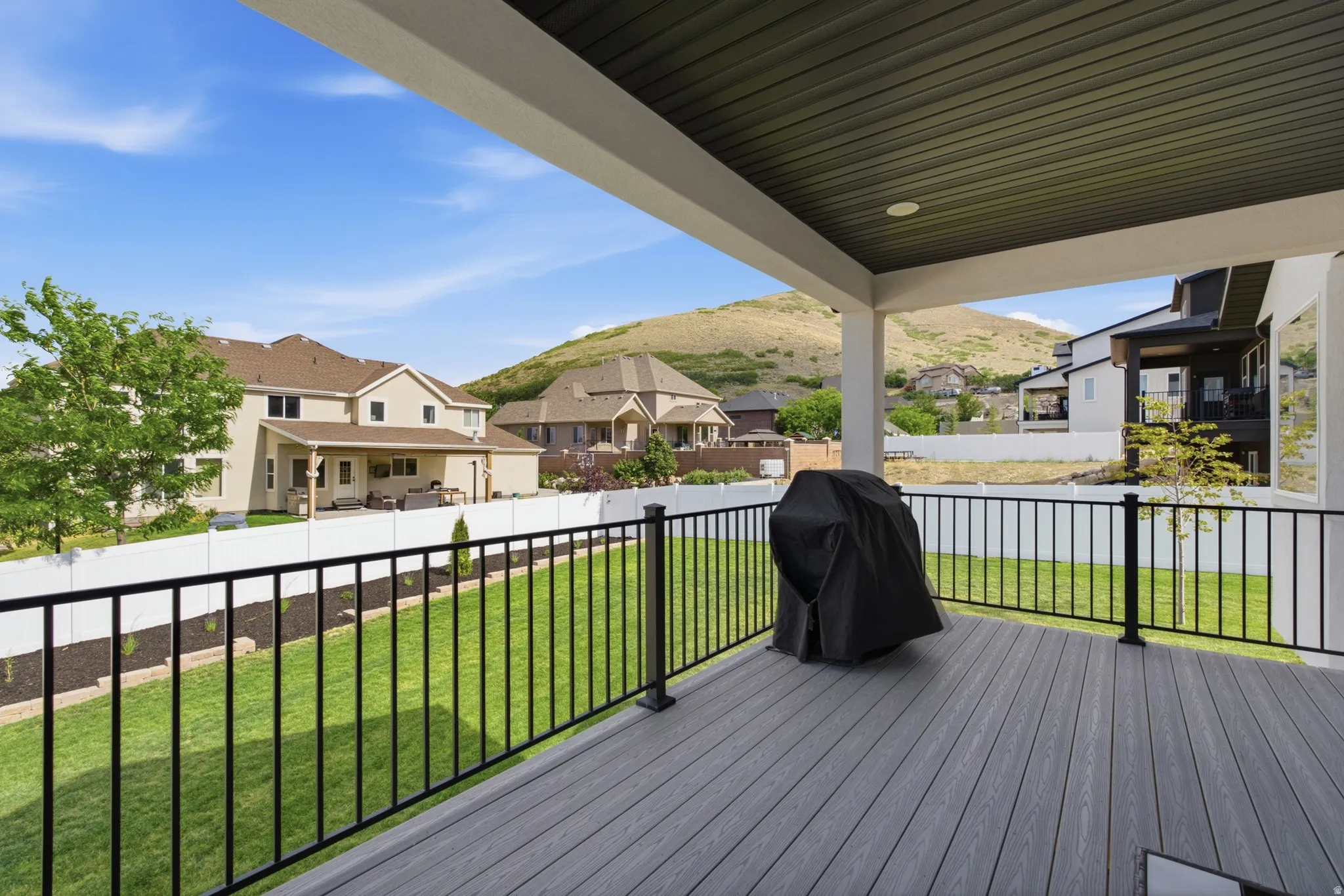 Covered outdoor deck with composite decking, black metal railings, and a slatted ceiling with recessed lighting