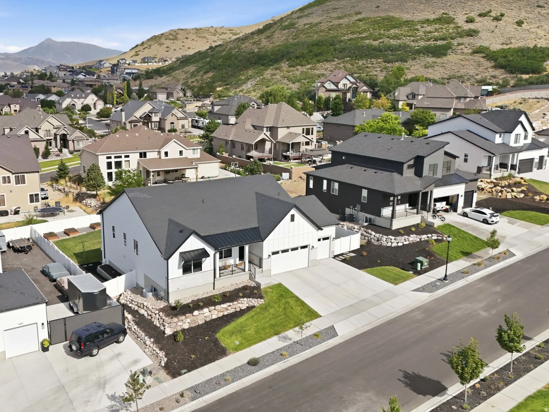 Modern farmhouse-style residence with a dark gray roof and white siding, featuring a two-car garage and a landscaped front yard with decorative rock walls
