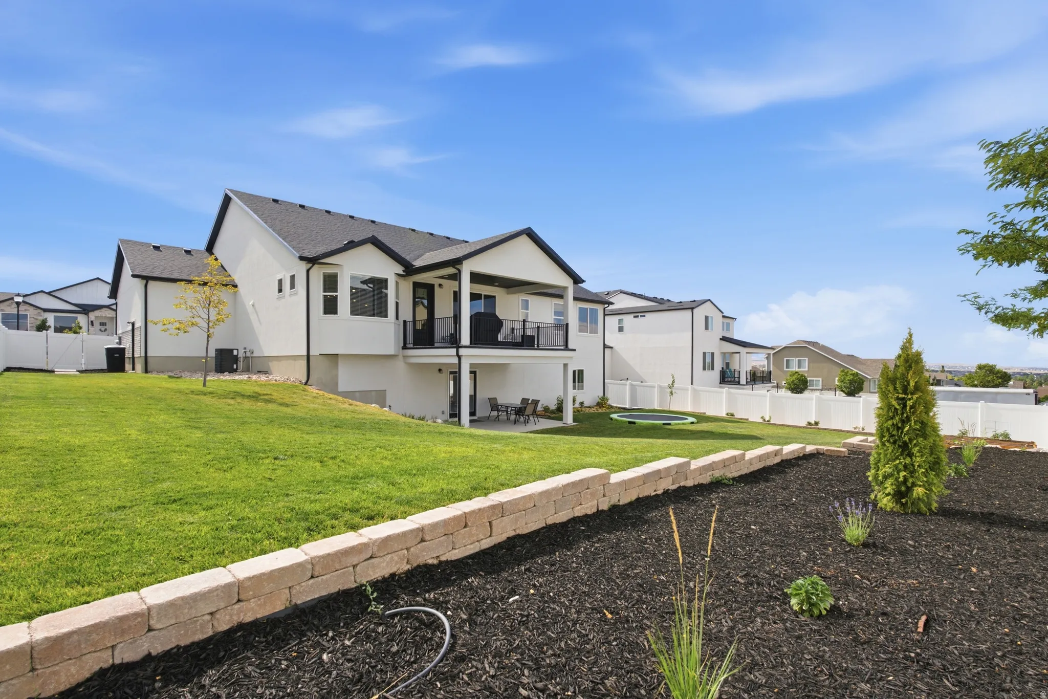 Expansive backyard featuring a large green lawn, tiered landscaping with a retaining wall, and a covered balcony