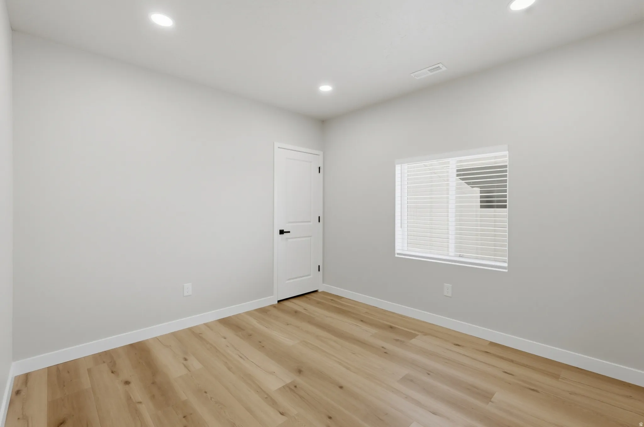 Neutral-toned room featuring wood-finish flooring, recessed lighting, and a window with blinds