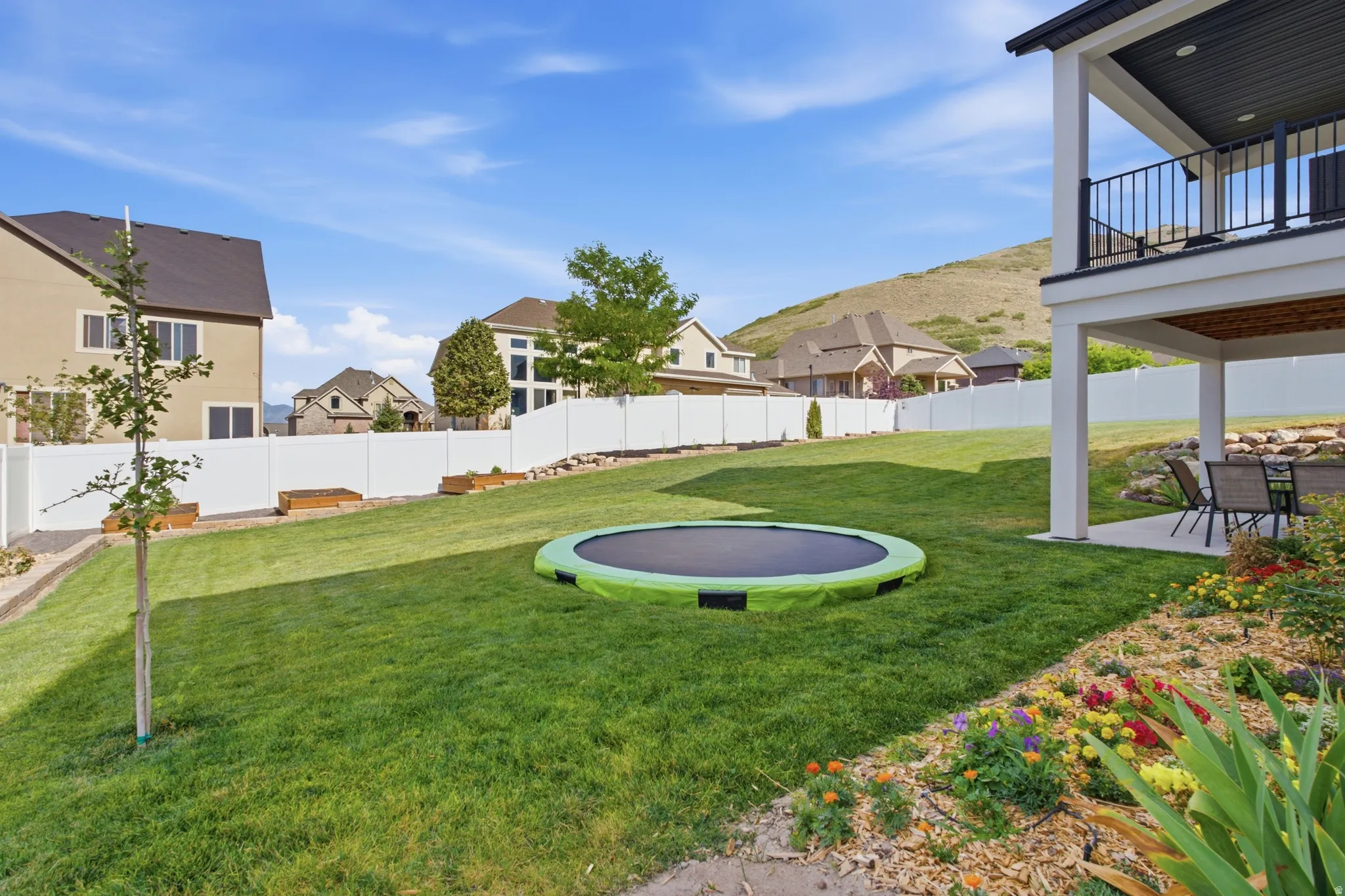 Expansive terraced backyard featuring a manicured lawn, established landscaping beds, and a white perimeter fence