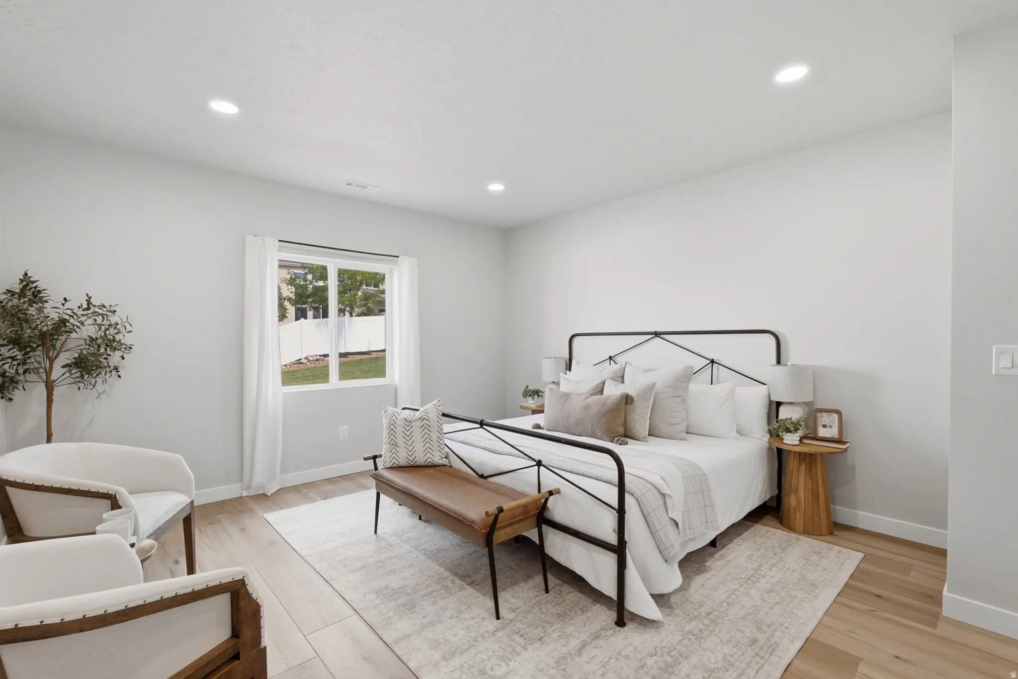Large bright ADU bedroom with recessed lighting, light wood-finish flooring, and a large window overlooking a fenced yard