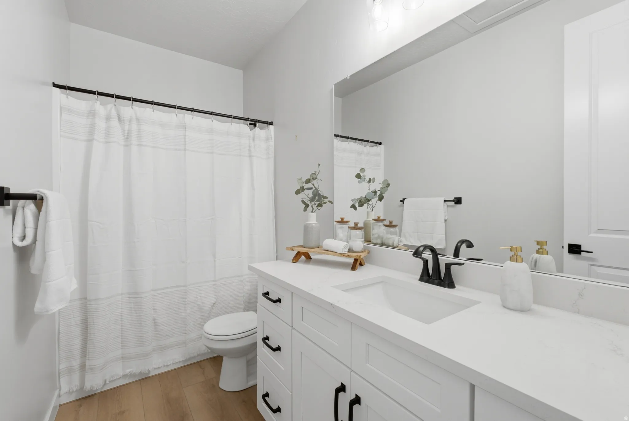Full Bathroom featuring a large single vanity with a white quartz countertop and integrated sink, matte black faucet, and white shaker-style cabinetry with black hardware