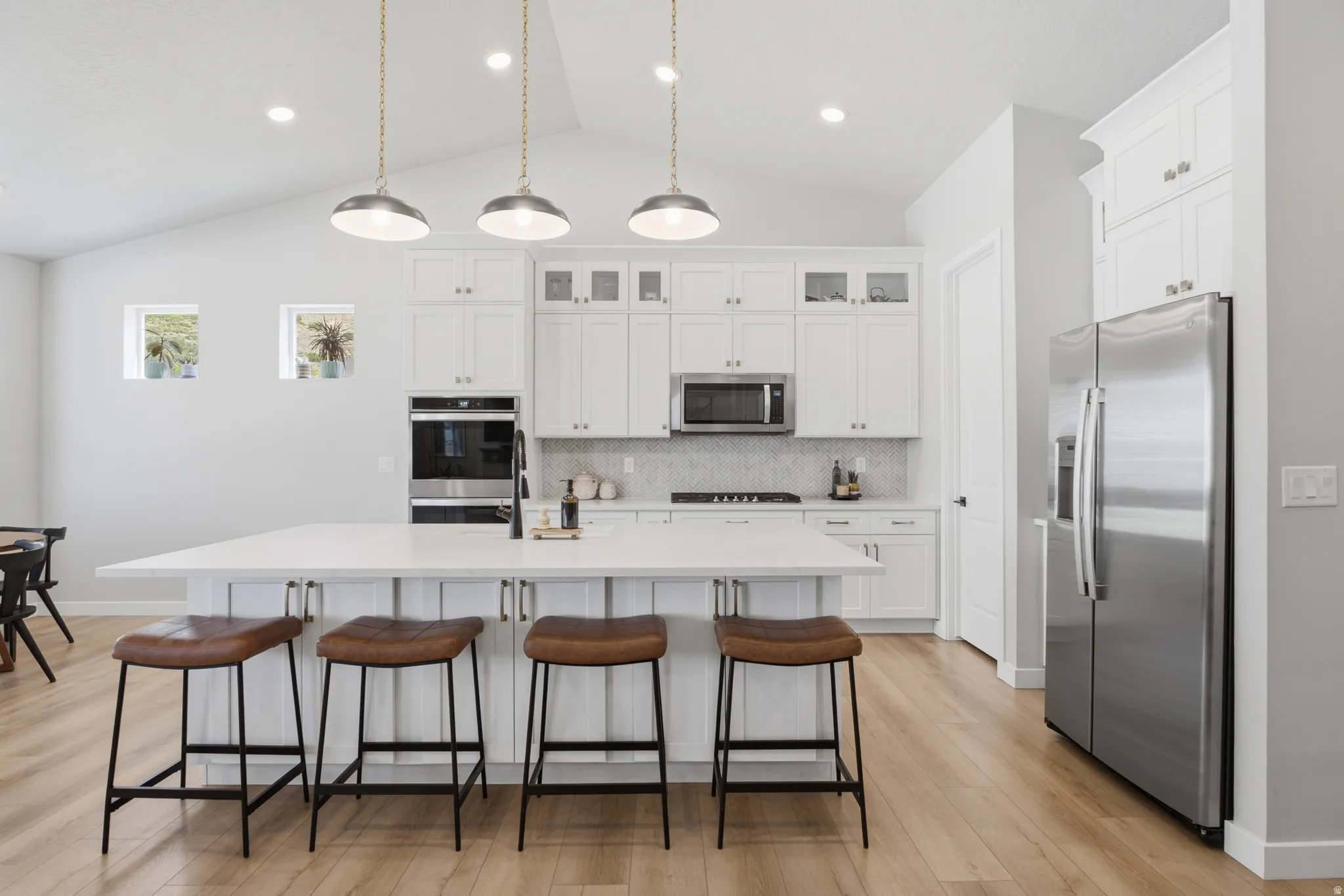 Modern kitchen featuring a large central island with seating, stainless steel appliances, white cabinetry with glass-front accents, and wood-finish flooring