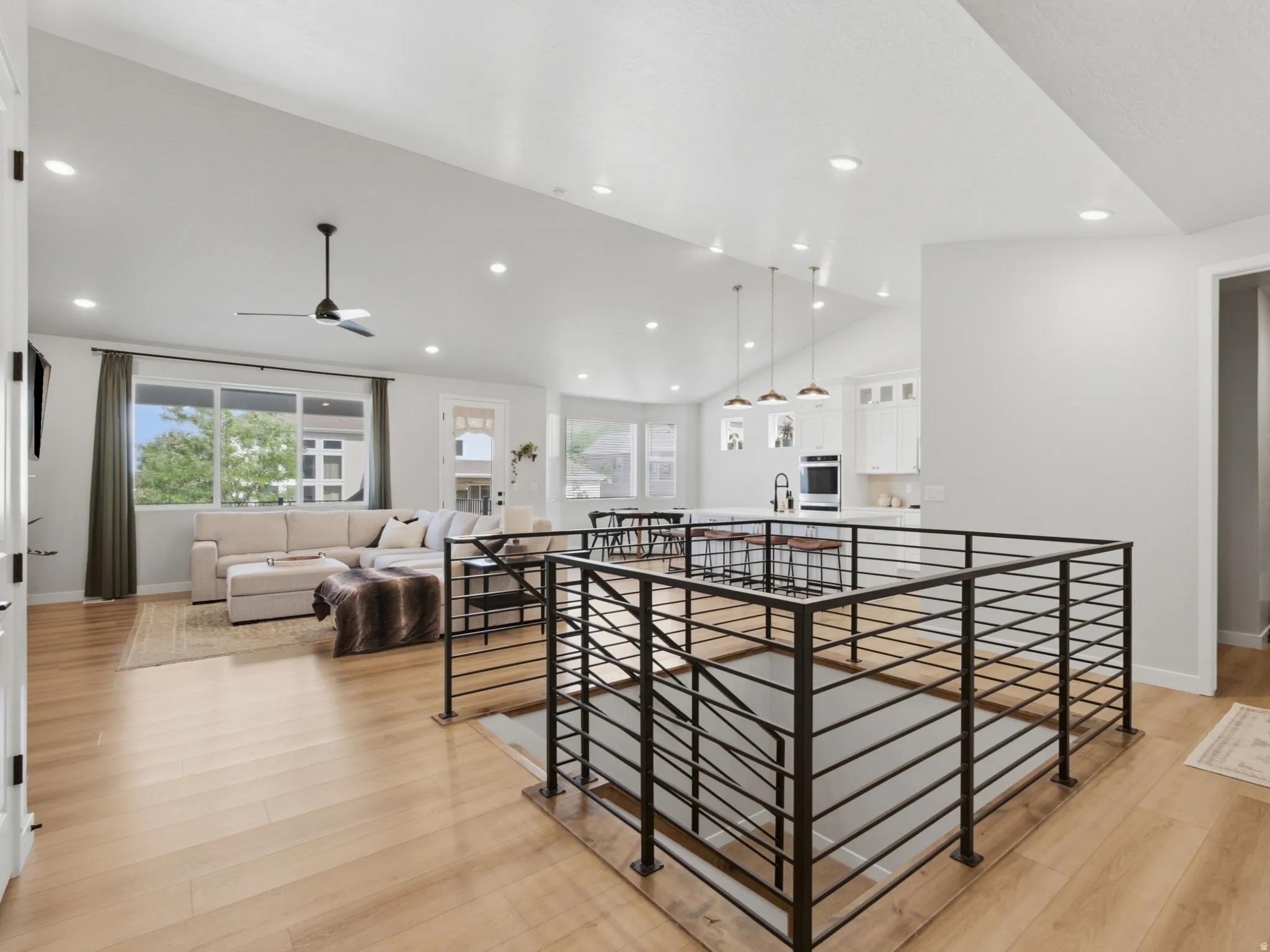 Open-concept living area with wood-finish flooring, recessed lighting, and a contemporary black metal balustrade