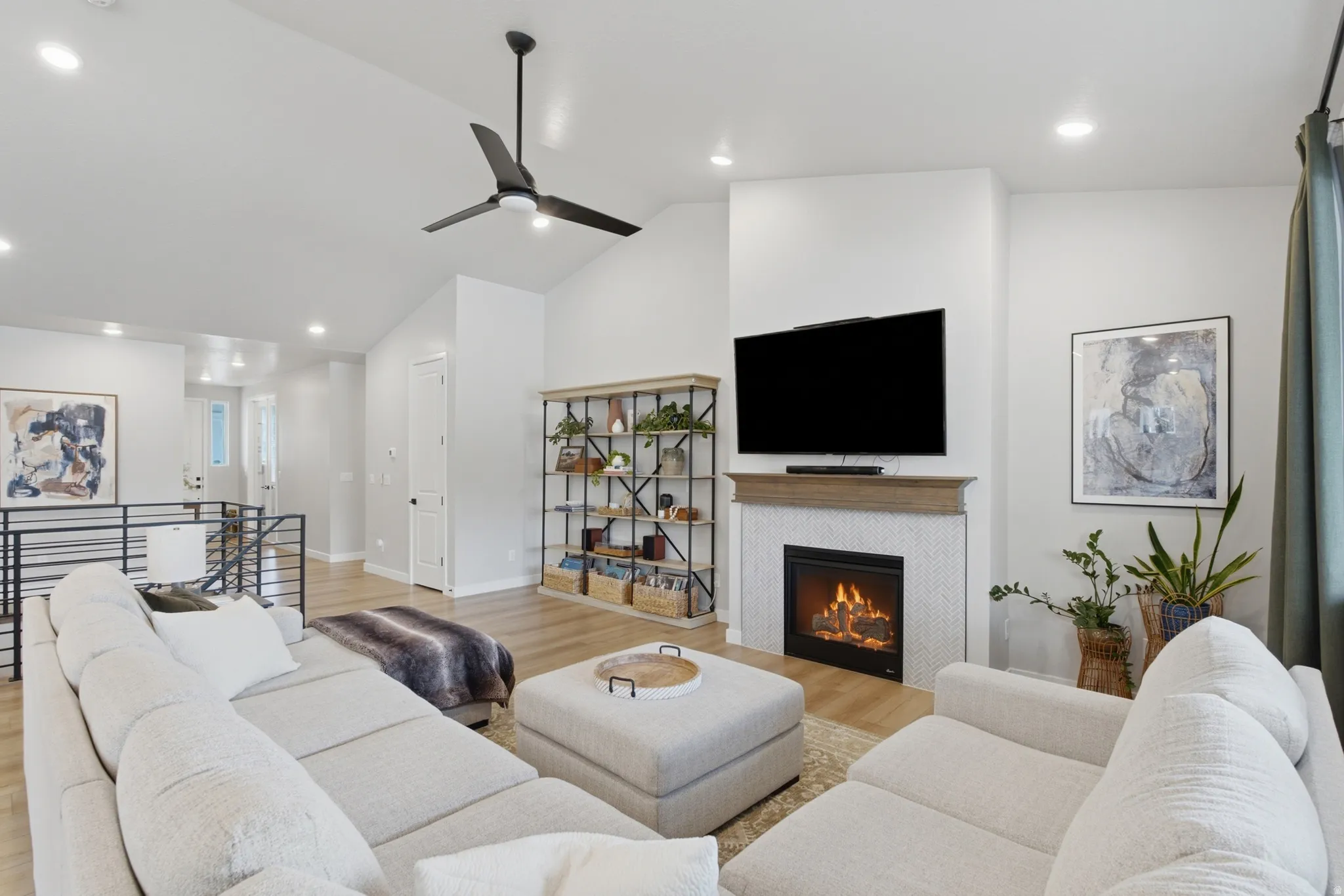 Vaulted ceiling living area featuring wood-finish flooring, a contemporary fireplace with tile surround, a dark metal ceiling fan, and recessed lighting