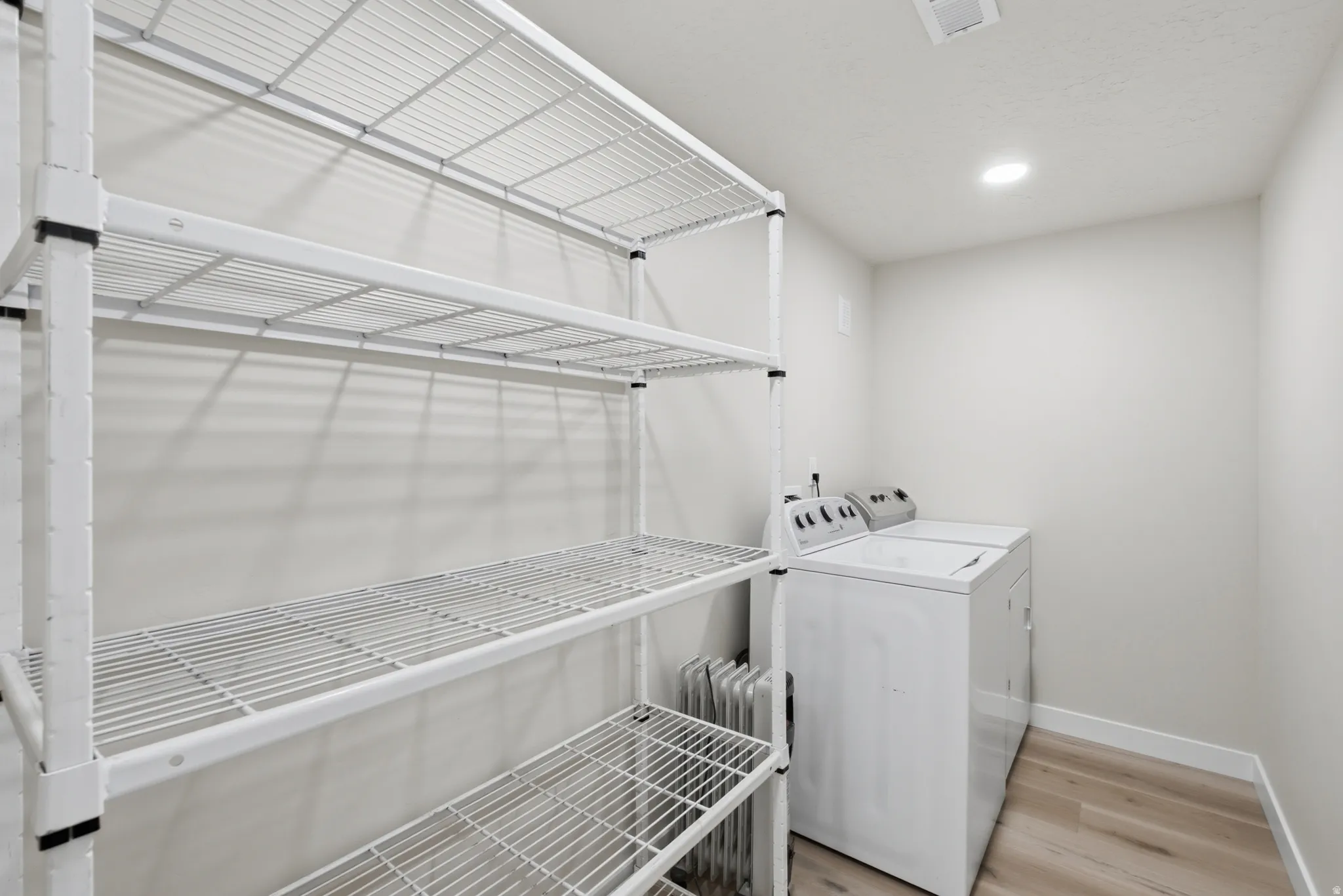 ADU Utility area featuring extensive wire shelving, light wood-finish flooring, recessed lighting, and a white baseboard trim