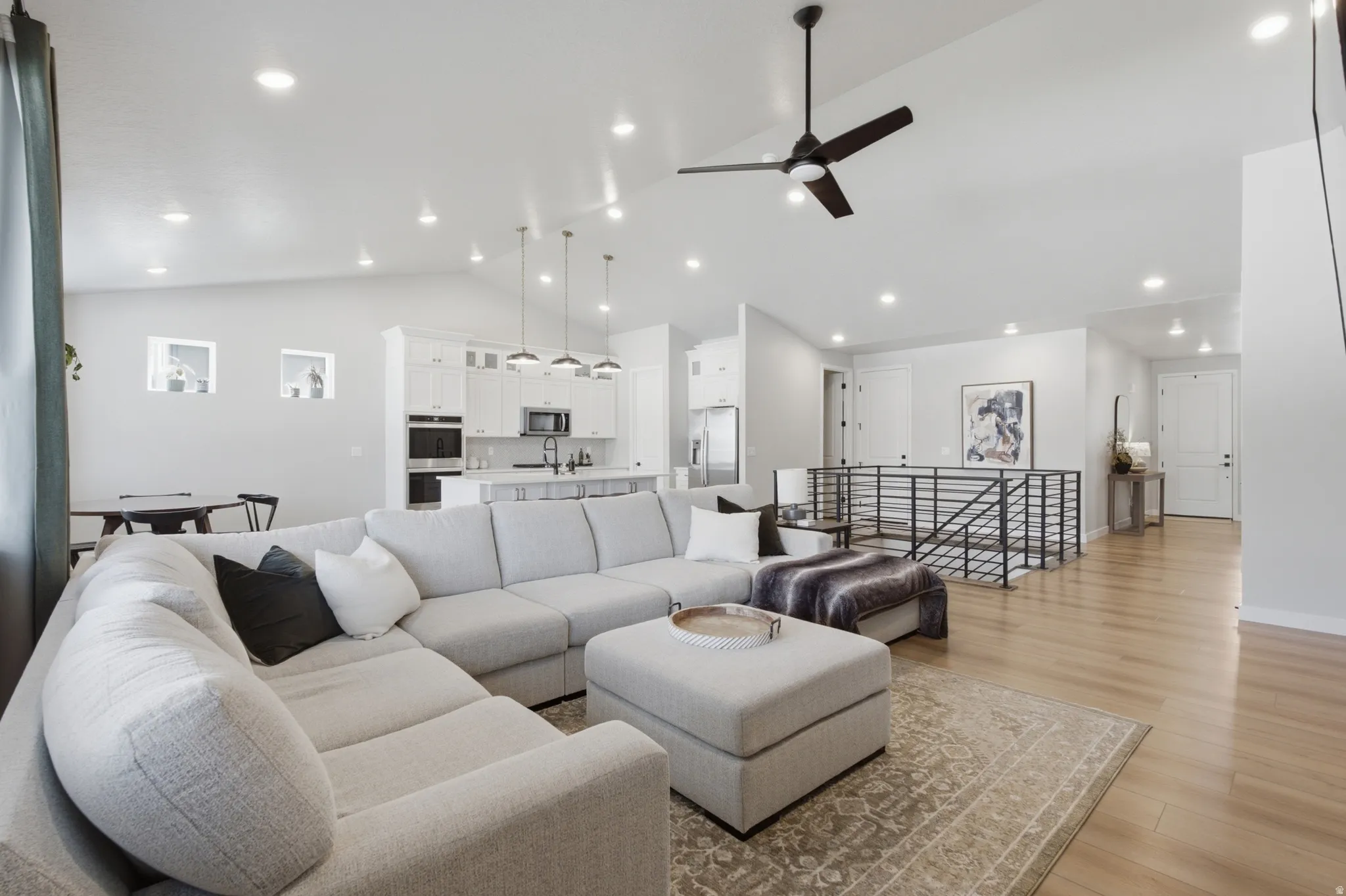 Open-concept living space featuring vaulted ceilings, recessed lighting, wood-finish flooring, a contemporary ceiling fan, and a kitchen with white cabinetry and pendant lighting
