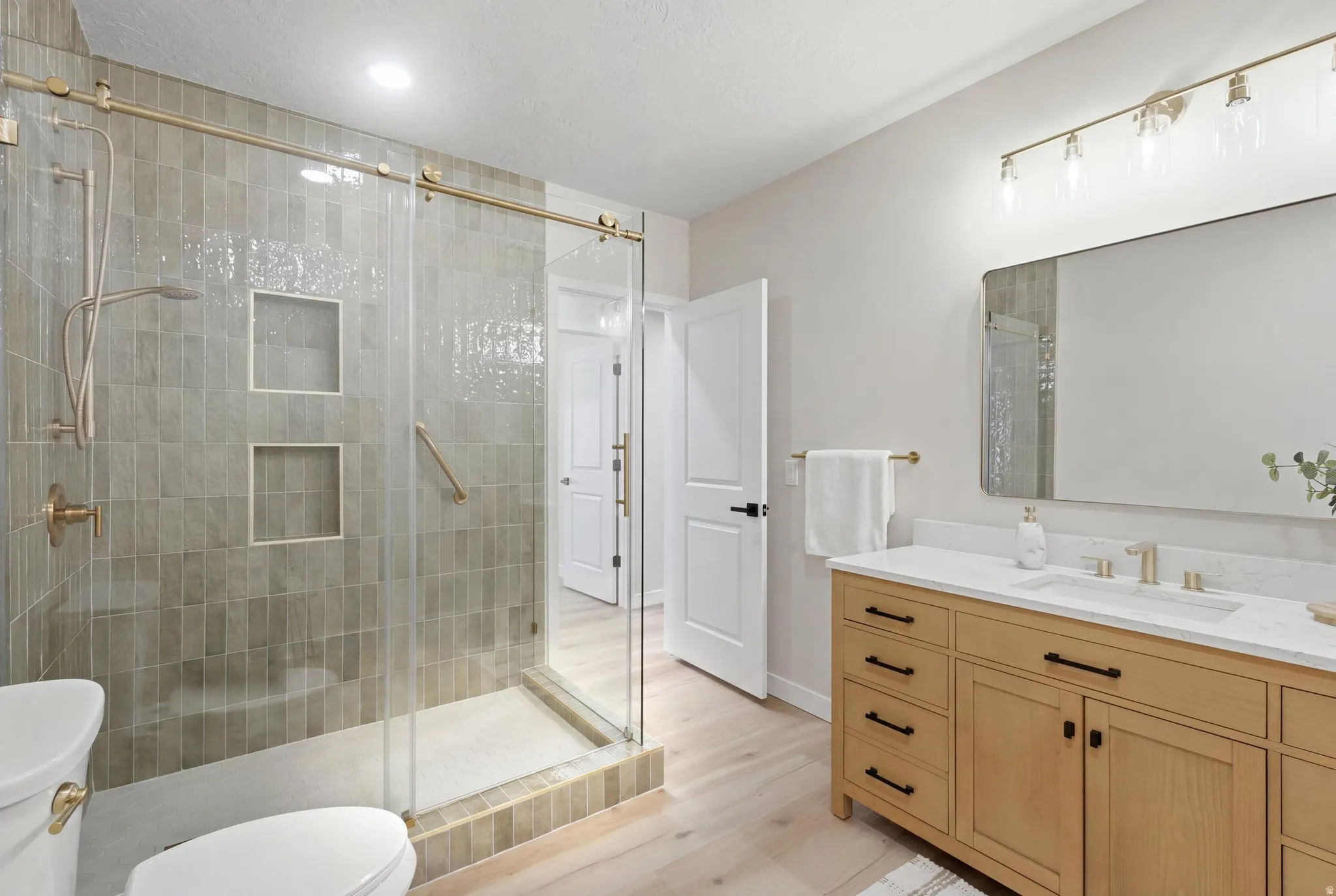 ADU Contemporary bathroom featuring a spacious glass-enclosed shower with custom vertical tile, dual shower niches, and gold-tone fixtures