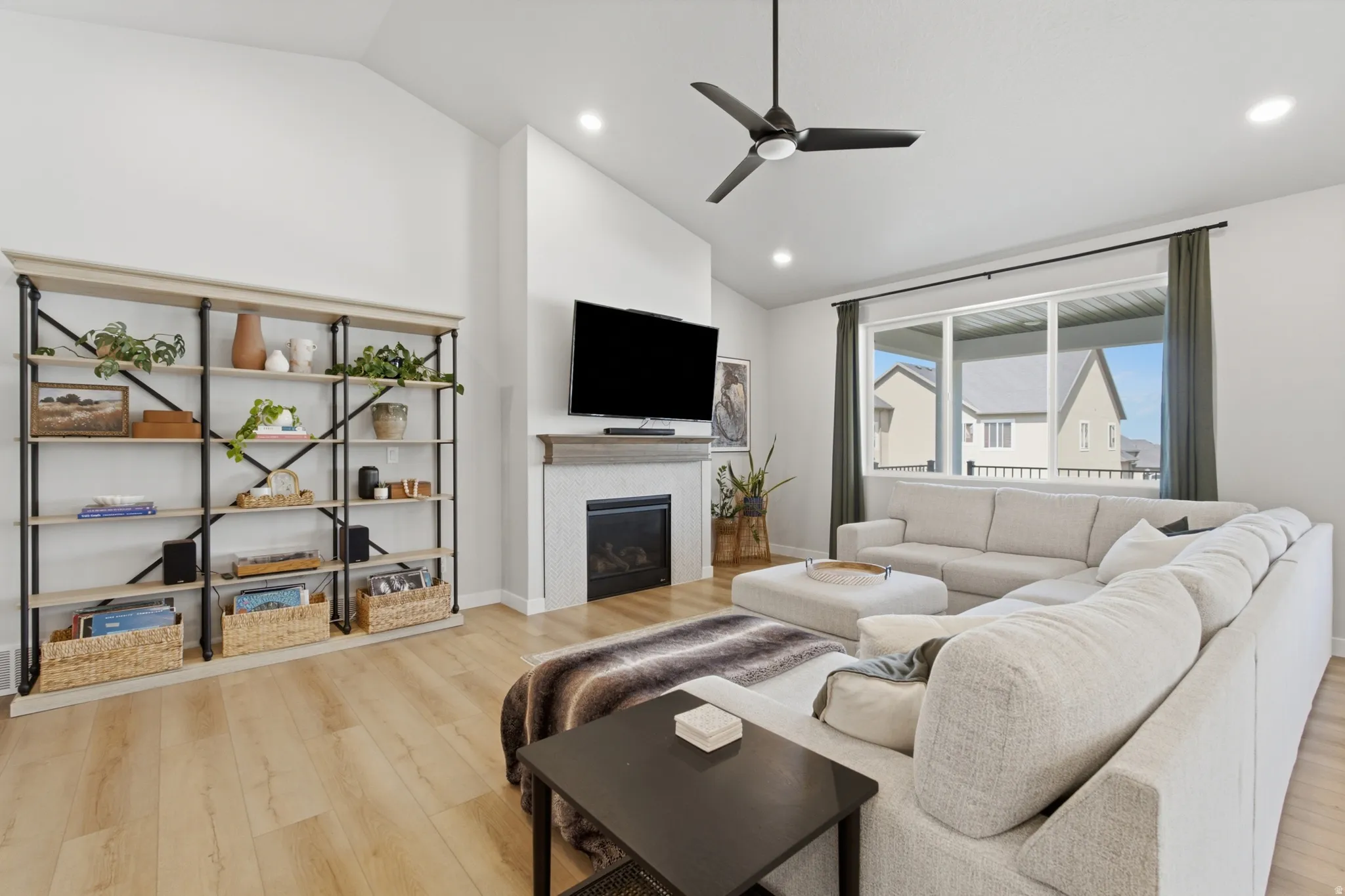 Spacious living area featuring light wood-finish flooring, a contemporary fireplace with a gray mantel, and a multi-pane window