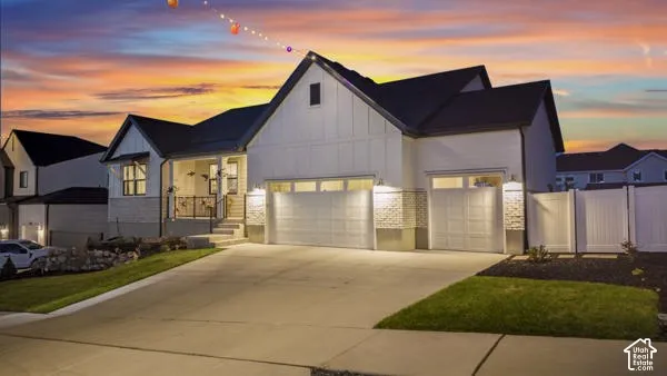 Modern farmhouse exterior with a covered porch, attached two-car garage, and white panel fencing