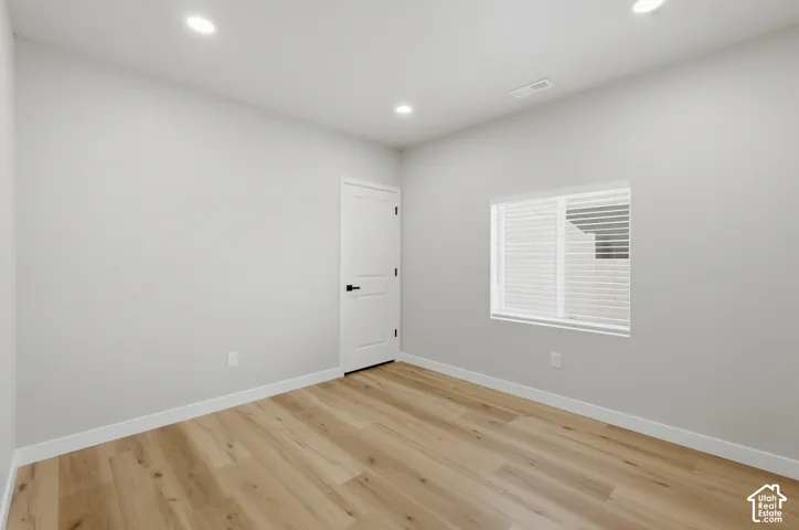 Neutral-toned room featuring wood-finish flooring, recessed lighting, and a window with blinds