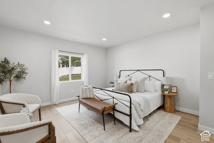 Large bright ADU bedroom with recessed lighting, light wood-finish flooring, and a large window overlooking a fenced yard