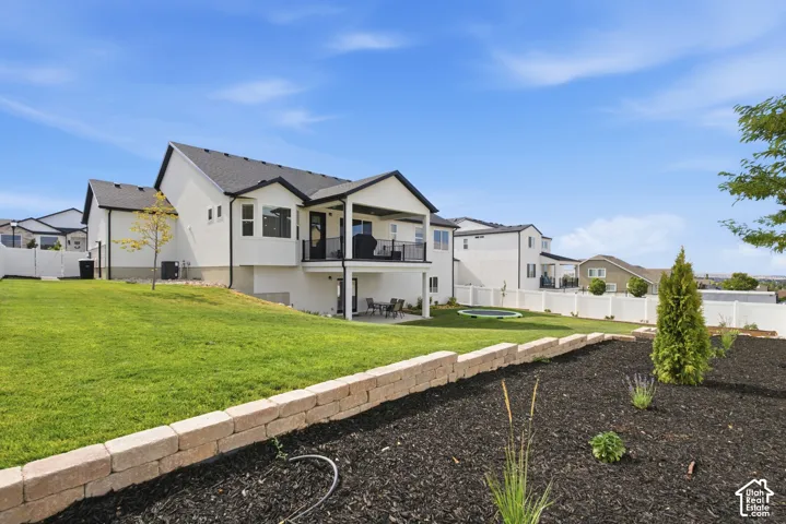 Expansive backyard featuring a large green lawn, tiered landscaping with a retaining wall, and a covered balcony