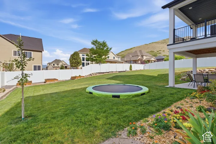Expansive terraced backyard featuring a manicured lawn, established landscaping beds, and a white perimeter fence