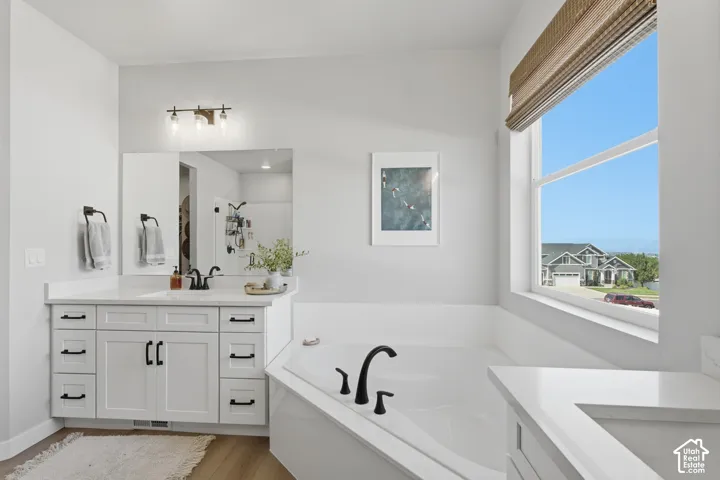 Ensuite Bathroom featuring a built-in corner soaking tub with a black-finish faucet, a large window with a woven shade, and a vanity with white cabinetry.