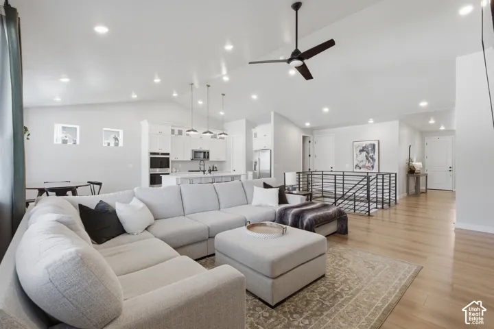 Open-concept living space featuring vaulted ceilings, recessed lighting, wood-finish flooring, a contemporary ceiling fan, and a kitchen with white cabinetry and pendant lighting