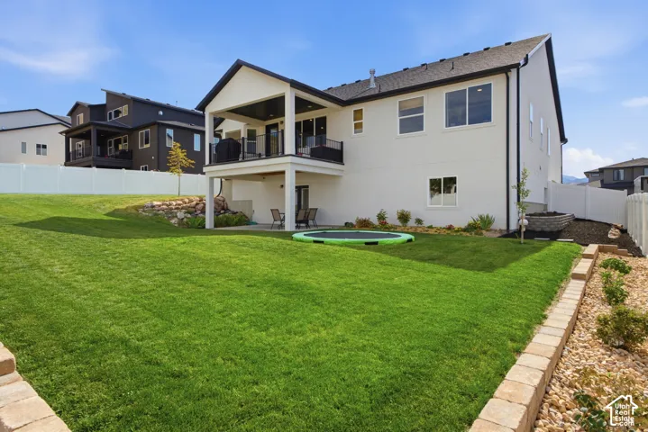 Spacious backyard with a vibrant green lawn, modern white siding exterior, covered upper-level deck with black railing, lower-level patio, and retaining wall landscaping