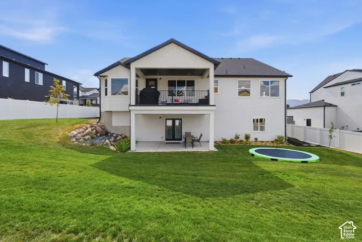 Rear exterior featuring a covered upper-level balcony, a lower-level patio, and an expansive lawn, ADU Entrance