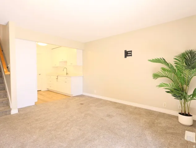 Neutral-toned carpeting extends throughout the main living area, complemented by a built-in wet bar featuring white cabinetry, a sink, and a gooseneck faucet