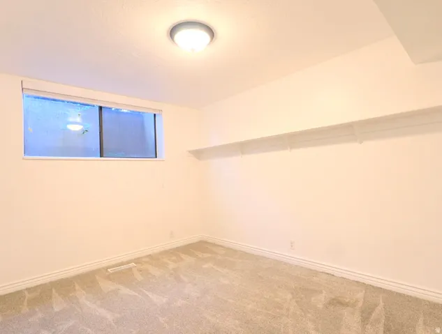 Room featuring neutral carpeting, a ceiling-mounted light fixture, white baseboards, and a horizontal window with a white blind
