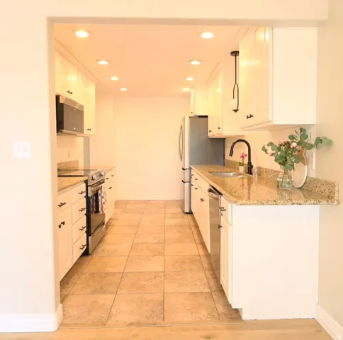 Galley kitchen featuring white cabinetry, granite countertops, stainless steel appliances, and recessed lighting