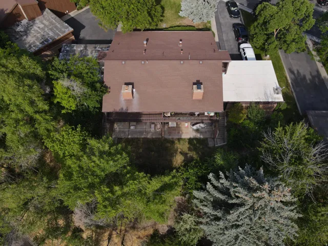 Aerial view of a property featuring a brown shingled roof, two visible brick chimneys, and a rear balcony