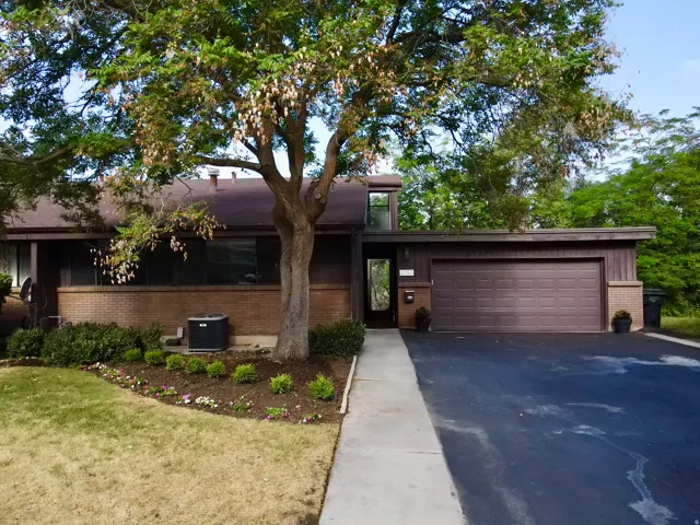 Ranch-style residence featuring a brick facade, integrated two-car garage, and mature front yard tree