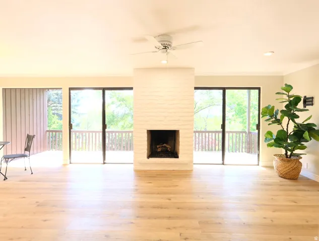 Open living area featuring wood-finish flooring, a white brick fireplace, and dual sliding glass doors opening to a private balcony with wood railings
