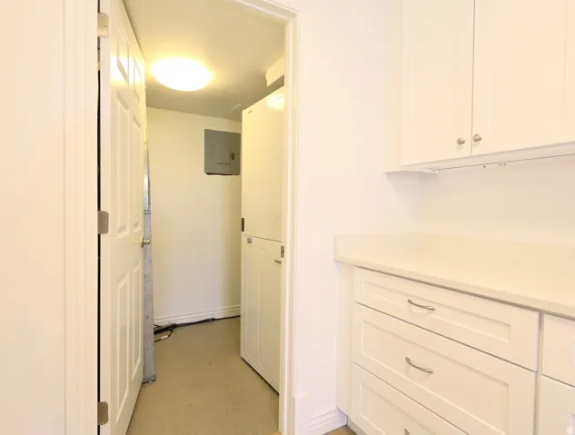 Laundry area featuring stacked appliances, overhead lighting, white cabinetry, integrated countertop, and recessed panel drawers