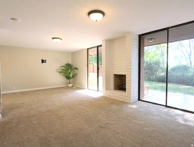 Spacious room featuring a white-painted brick fireplace, two large sliding glass doors, neutral carpeting, and recessed lighting