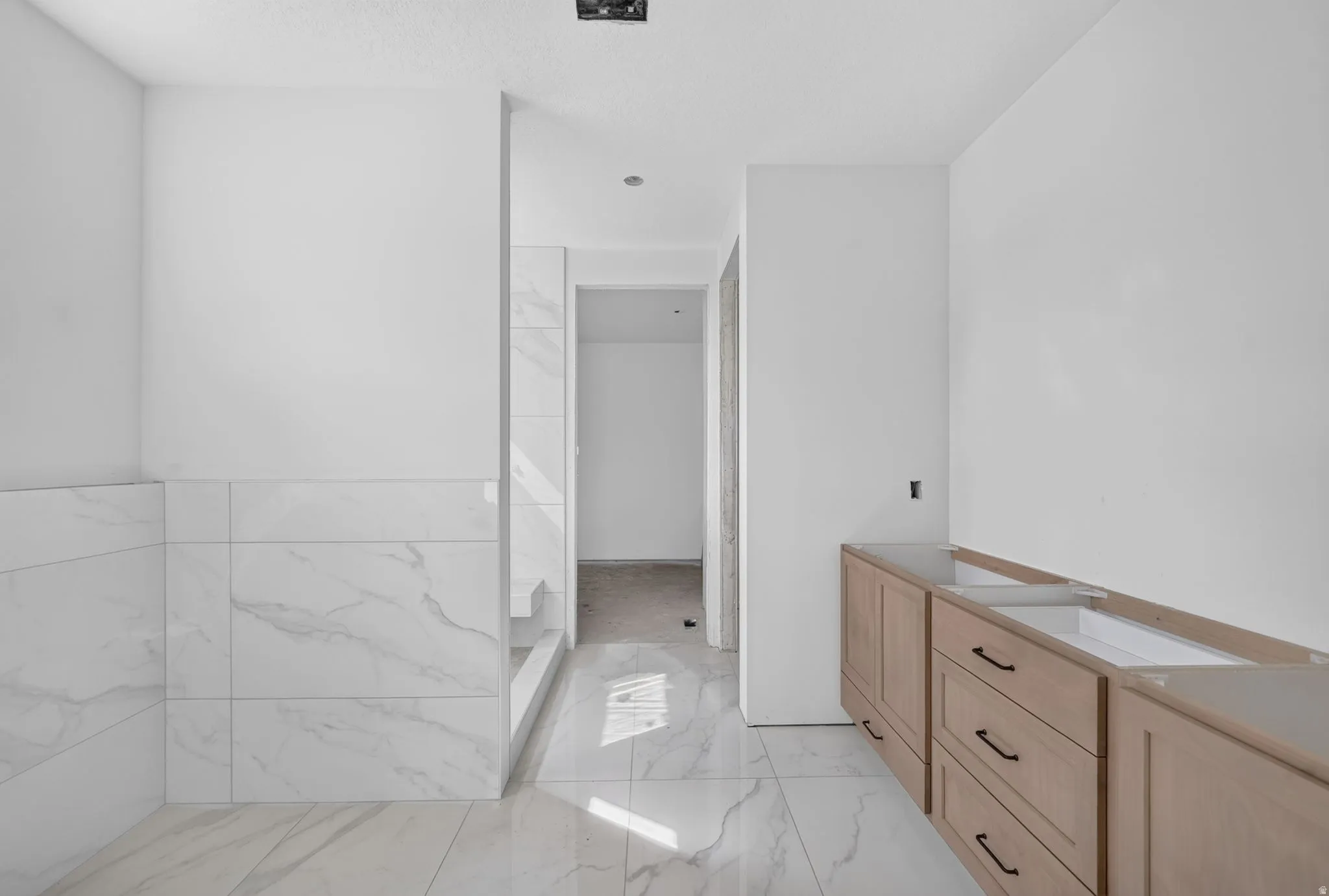 Spa-inspired primary bathroom featuring a walk-in shower with glass enclosure, polished marble-finish flooring throughout, dual vanity with wood cabinetry and integrated countertop, and abundant natural lighting from recessed ceiling fixtures