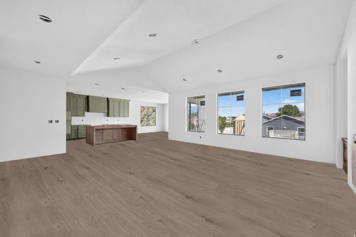 Vaulted ceiling with recessed lighting, wood-finish flooring, multiple windows, kitchen with green cabinetry, and a wood-finish island