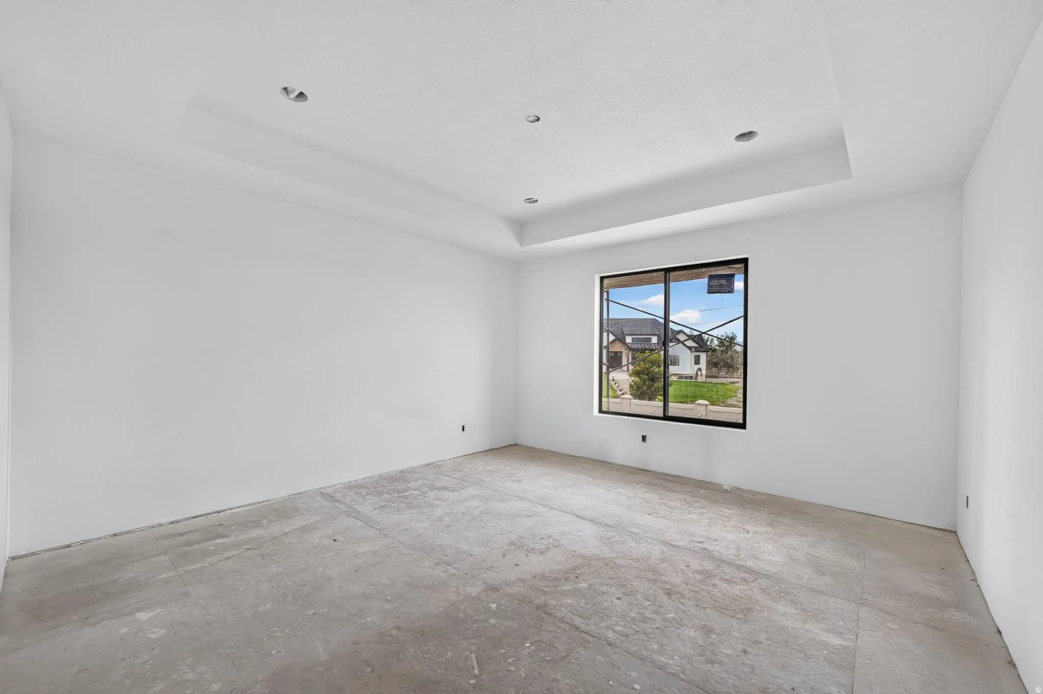 Tray ceiling with recessed lighting, large window with black framing, and concrete subfloor