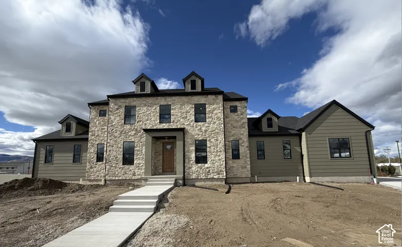 Multi-level exterior featuring light stone masonry, horizontal siding, dormer windows, and a covered entryway
