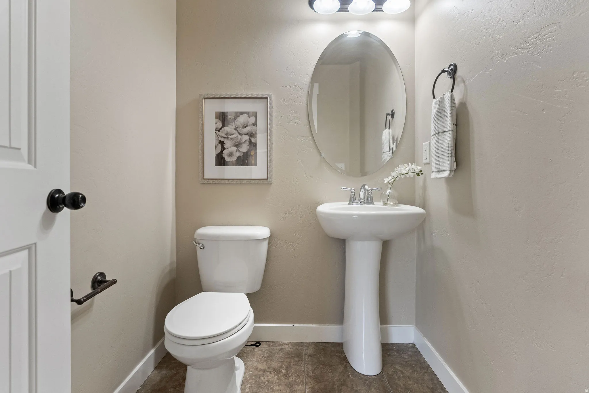 Compact powder room featuring a white pedestal sink, an oval wall-mounted mirror, and a three-bulb vanity light fixture