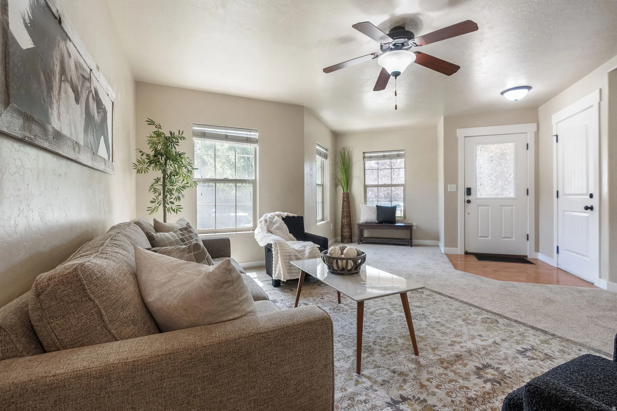 Living area featuring a ceiling fan with light fixture, multiple windows, and a wood-finish entry floor