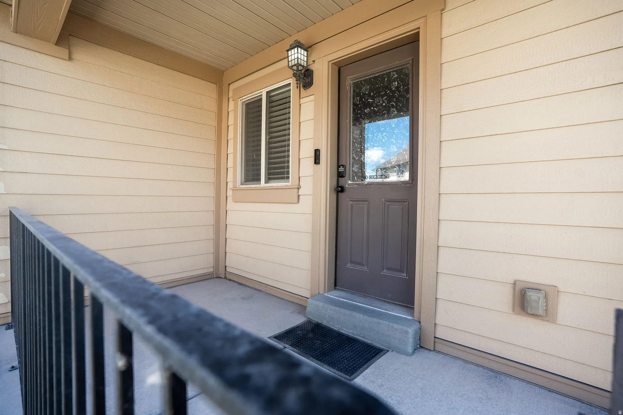 Front entry featuring a brown door with an integrated glass panel, a concrete porch, and a black wrought iron railing