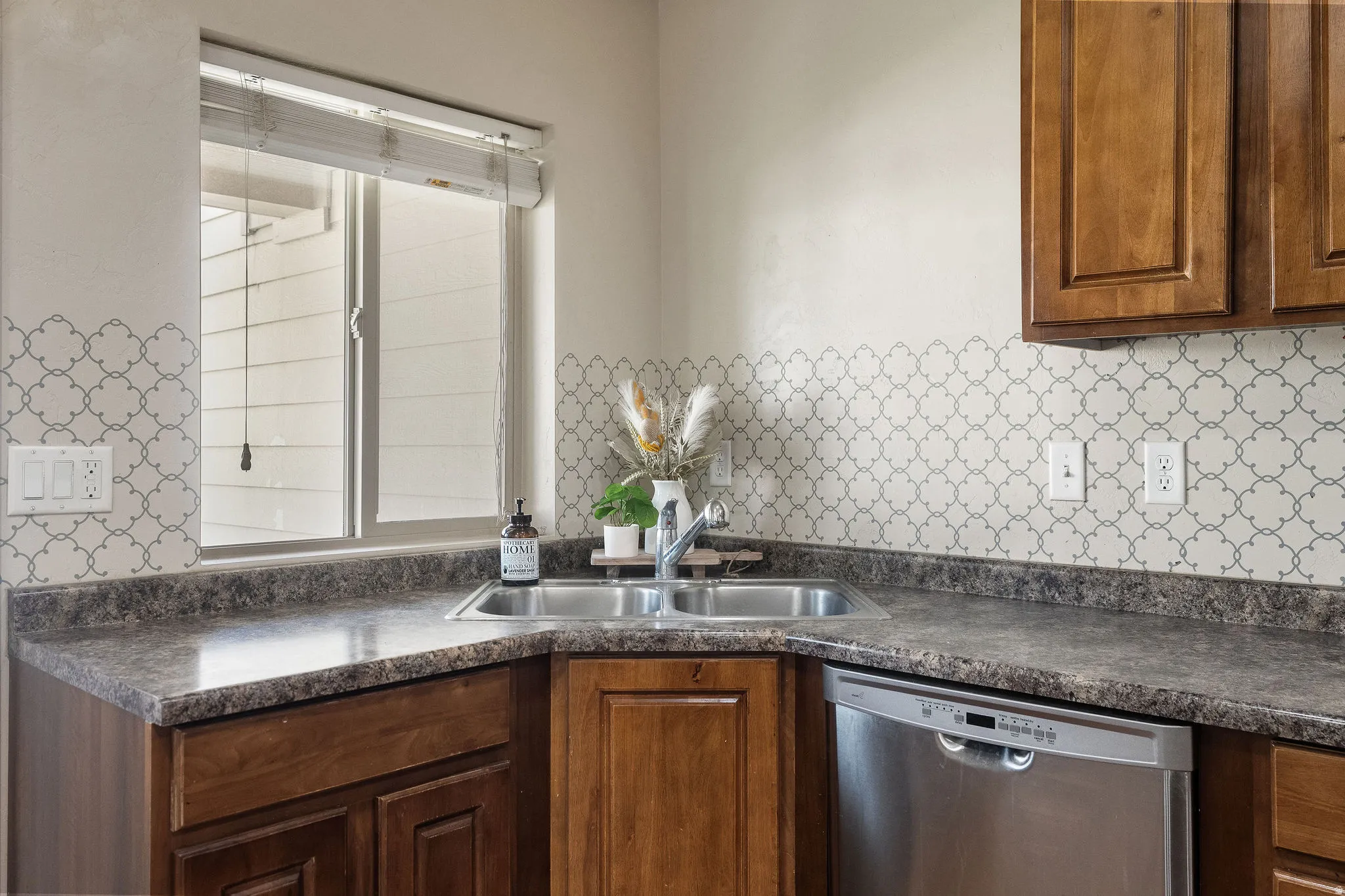 Kitchen sink area featuring a dual-basin stainless steel sink, a stainless steel dishwasher, and wood-finish cabinetry