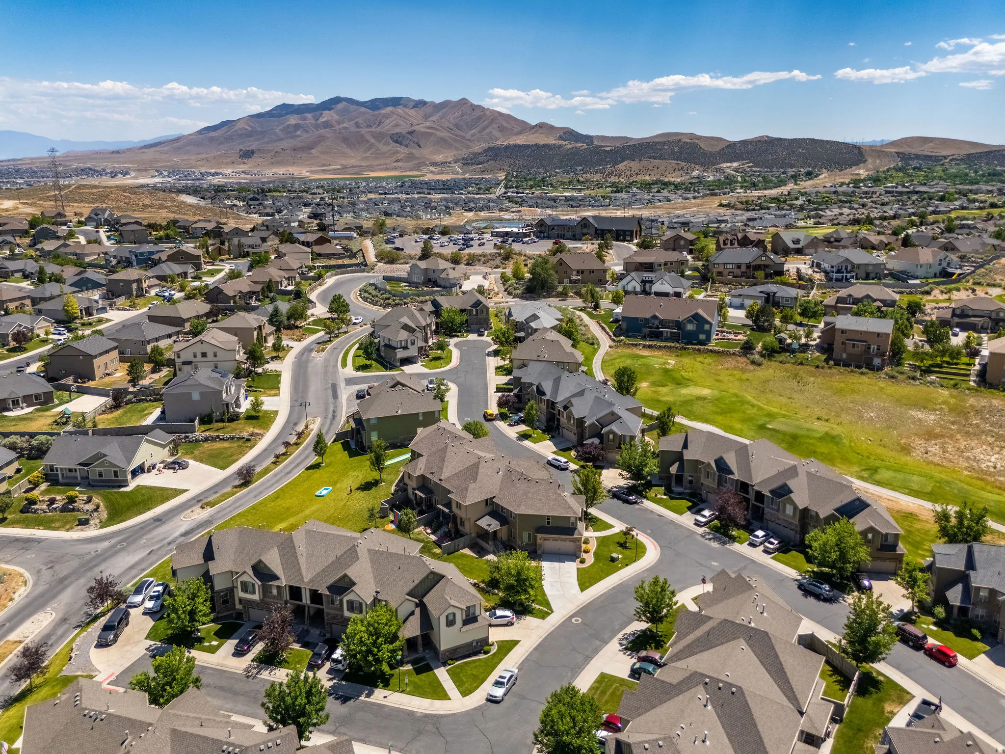 Aerial perspective of a residential neighborhood featuring diverse housing styles, paved streets, and green spaces