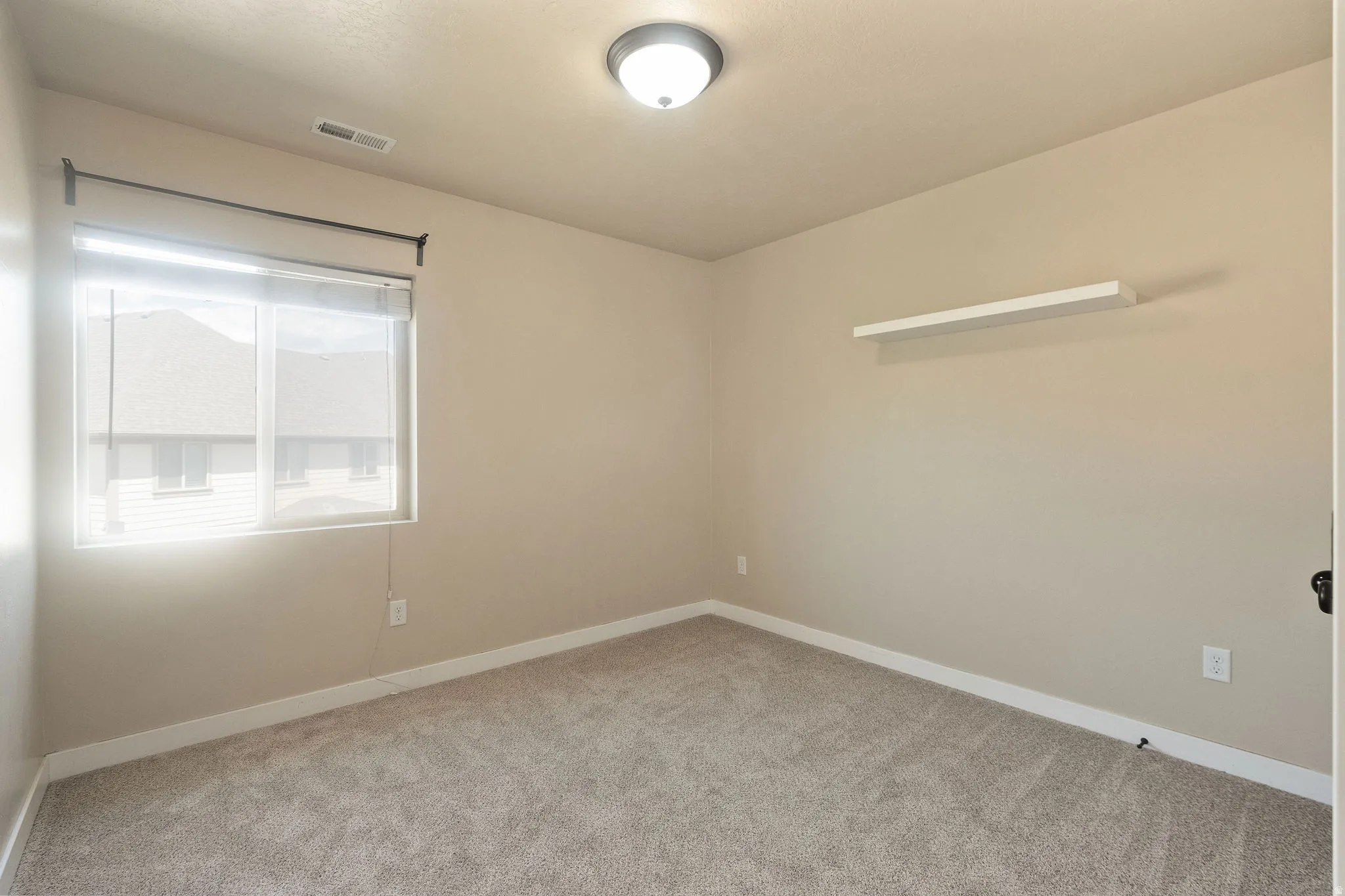 Spacious room featuring neutral carpet flooring, a single window with blinds, and a built-in wall shelf
