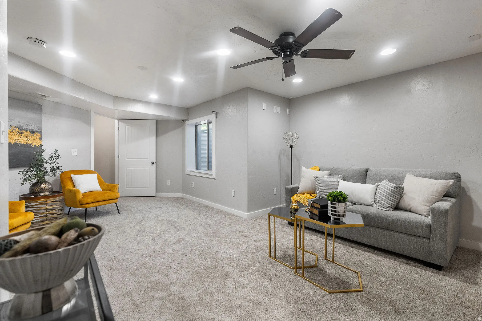 Spacious room featuring light gray textured walls, recessed ceiling lighting, a ceiling fan with dark blades, light gray carpeting, and a white two-panel door