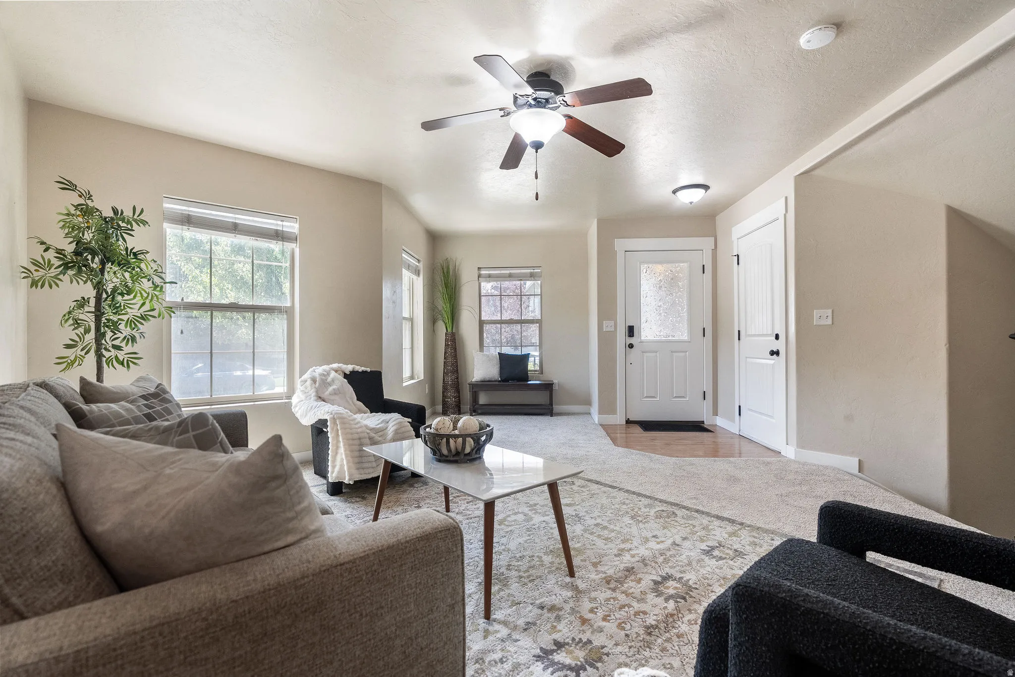 Bright living room featuring light-toned walls, a ceiling fan with integrated lighting, and multiple windows