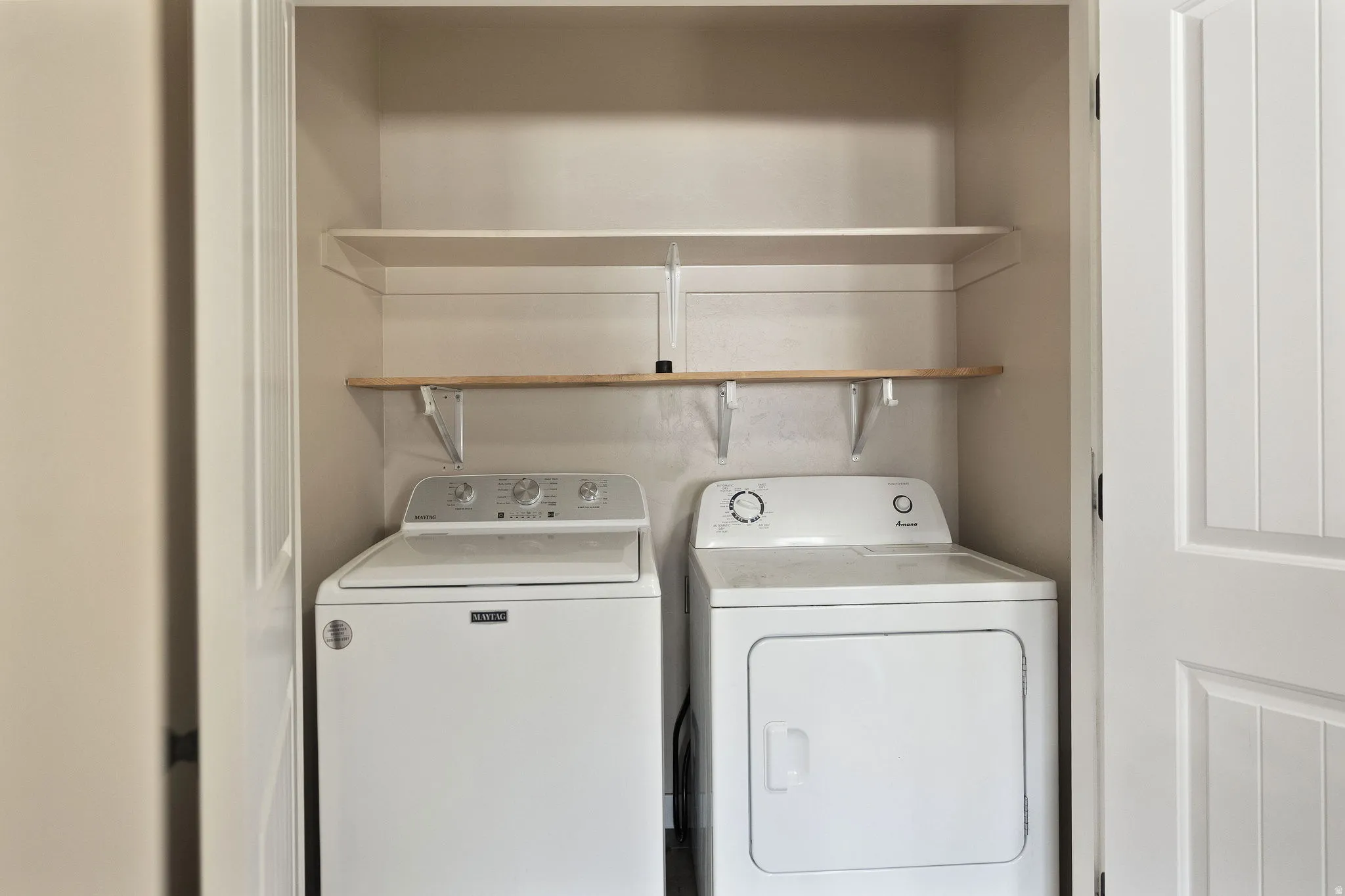 Dedicated laundry closet featuring a top-load washing machine, front-load dryer, and two built-in storage shelves