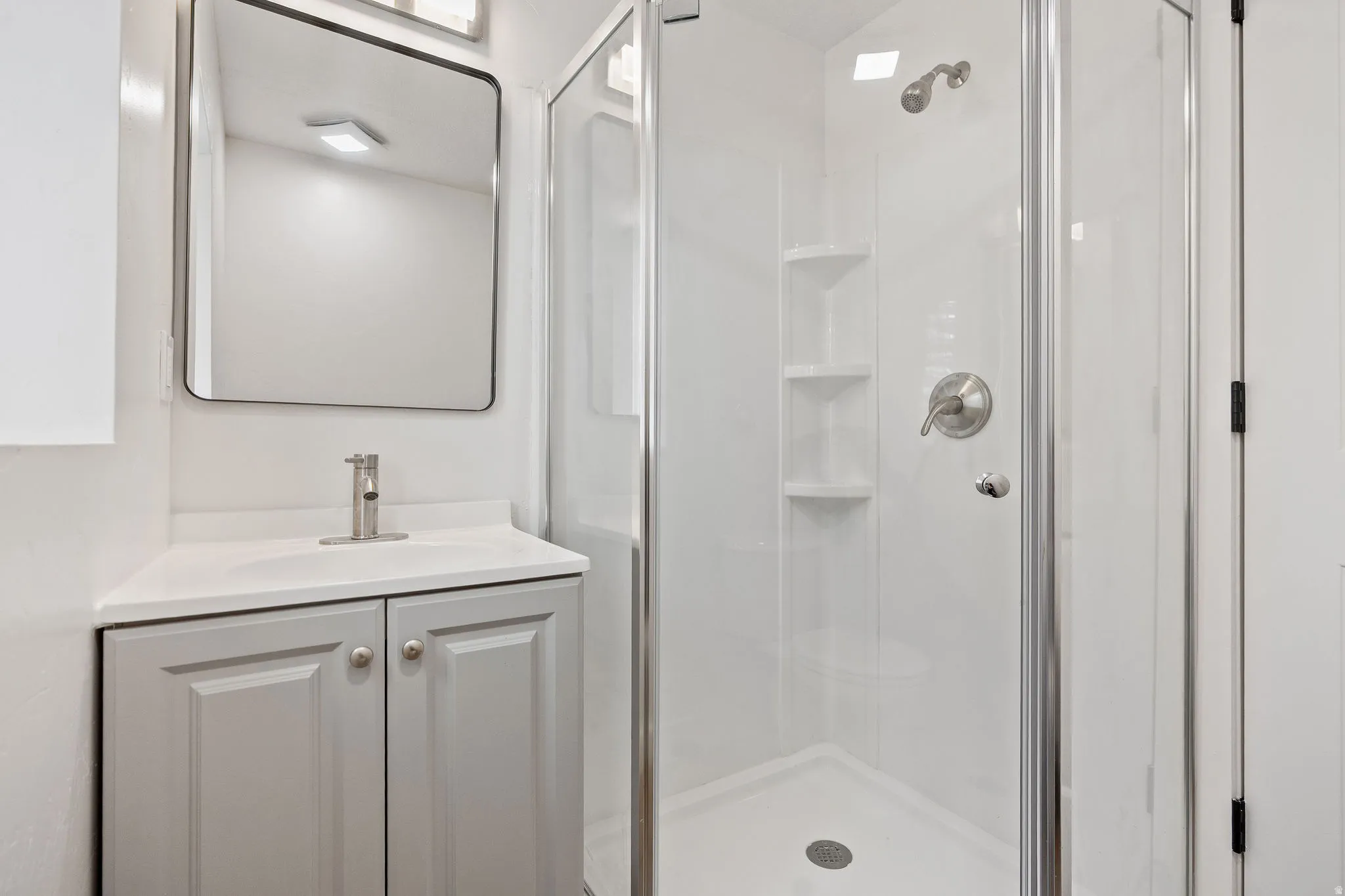 Modern bathroom featuring a glass-enclosed shower with integrated shelving, a sleek brushed nickel showerhead, and a coordinating single-handle faucet