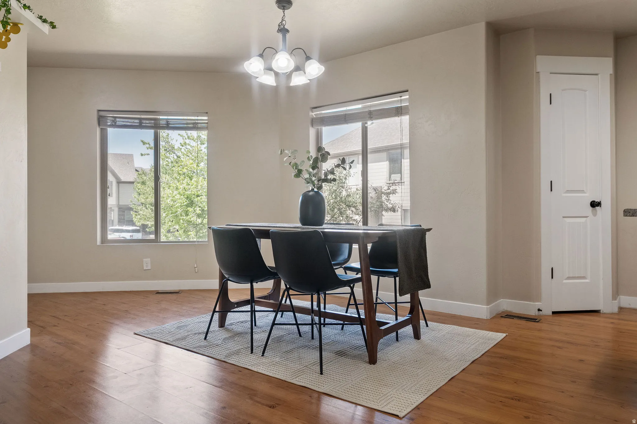 Dining area with wood-finish flooring, two large windows, and a five-light chandelier