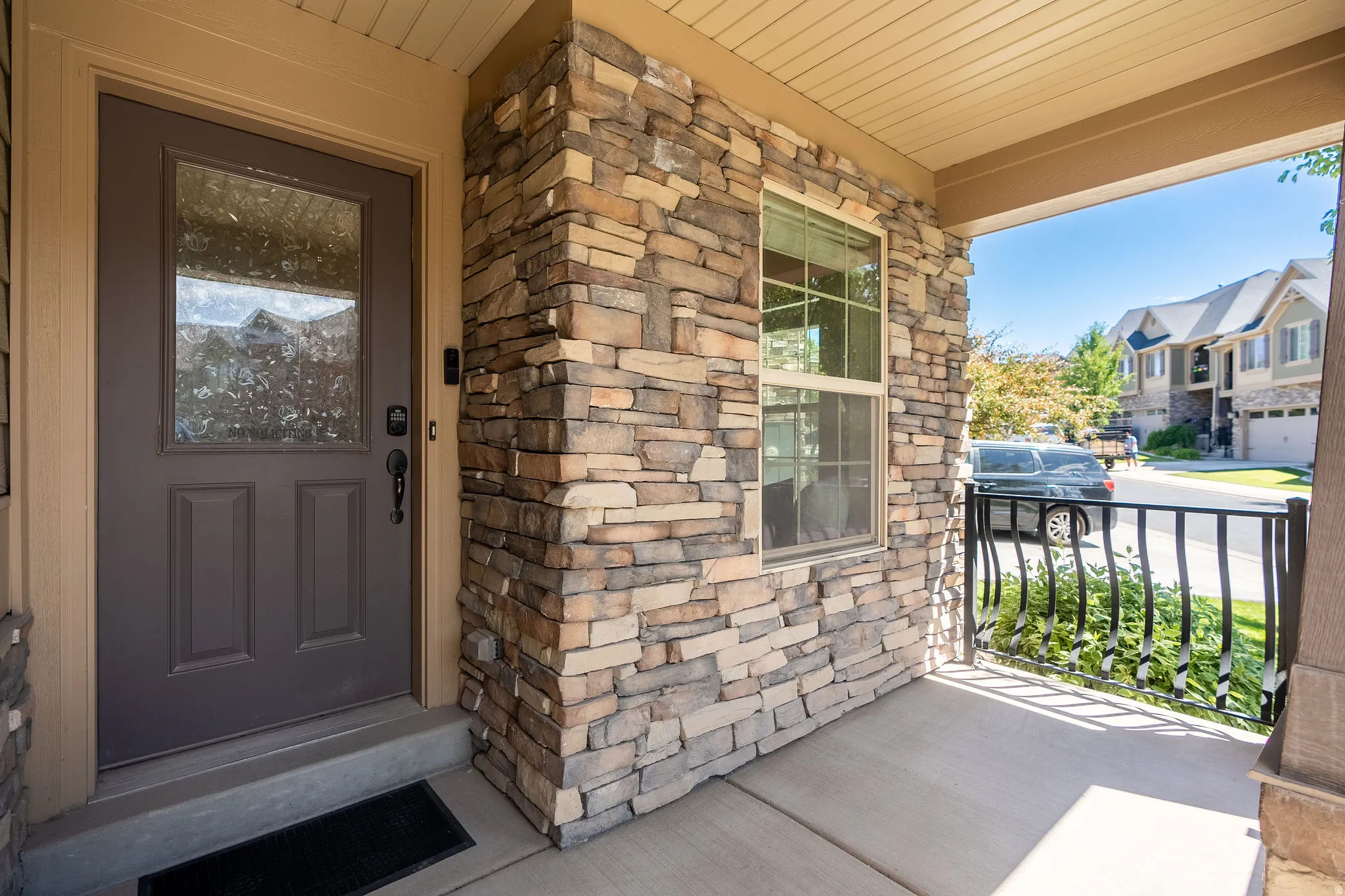 Inviting front porch featuring a stacked stone facade, a dark paneled entry door with an integrated window, a concrete porch floor, and black wrought iron railing