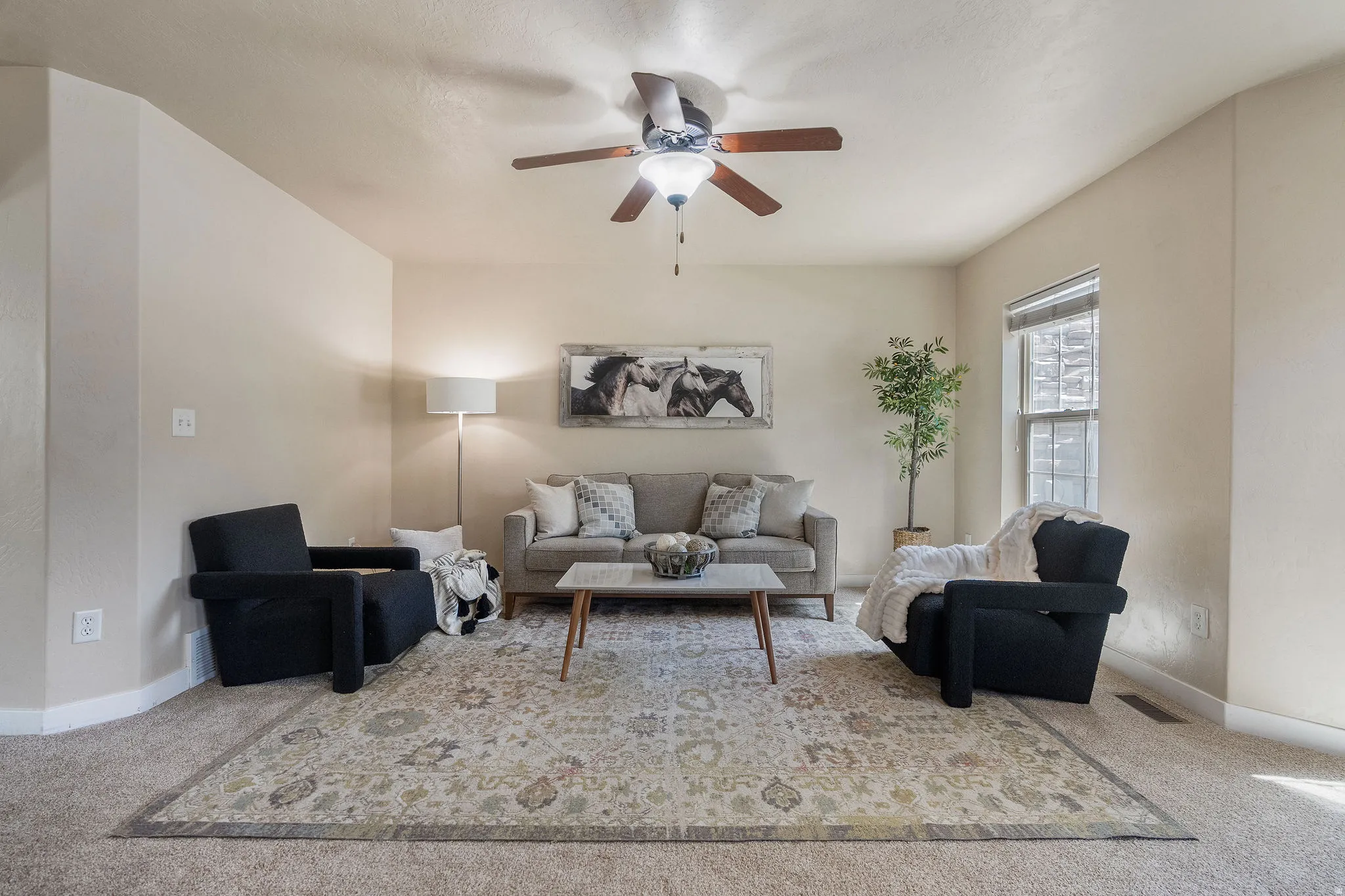 Carpeted living area featuring a ceiling fan with integrated lighting, neutral wall tones, and a window with blinds