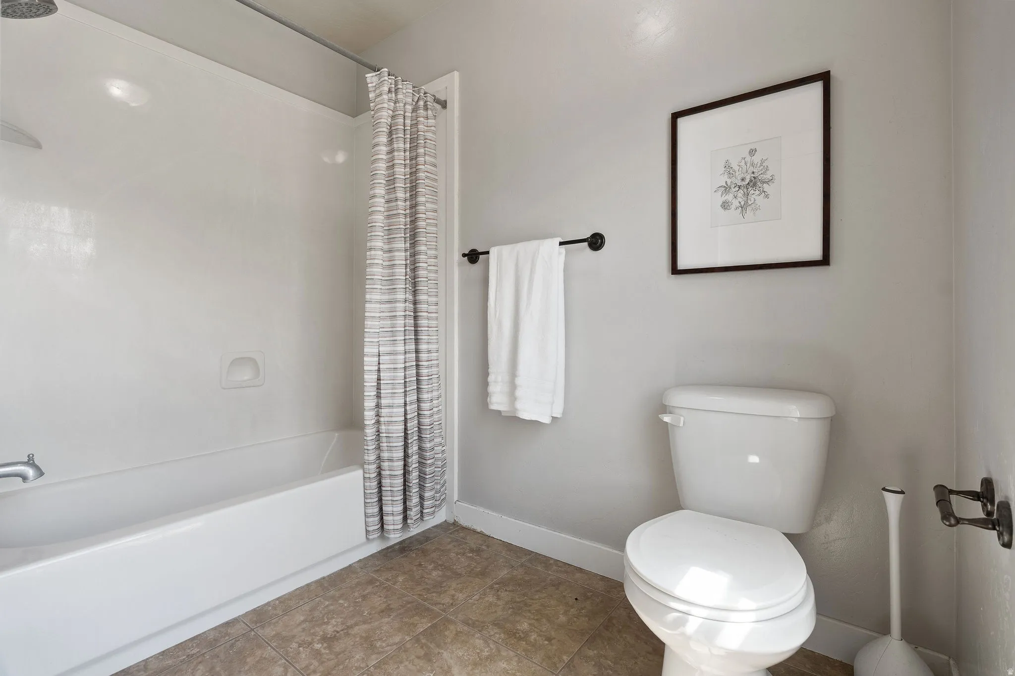 Bathroom featuring a white tub and shower combination, a standard toilet, and tiled flooring